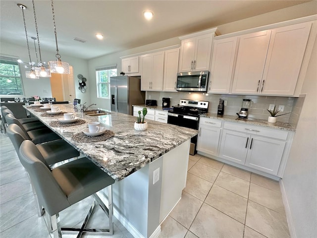 kitchen with appliances with stainless steel finishes, a sink, white cabinetry, and a kitchen bar