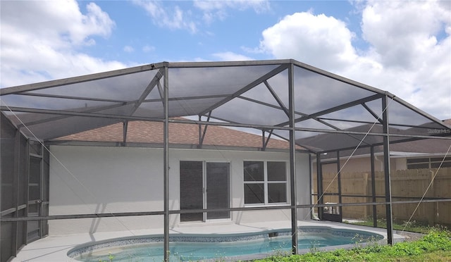 swimming pool featuring glass enclosure, a patio area, and fence