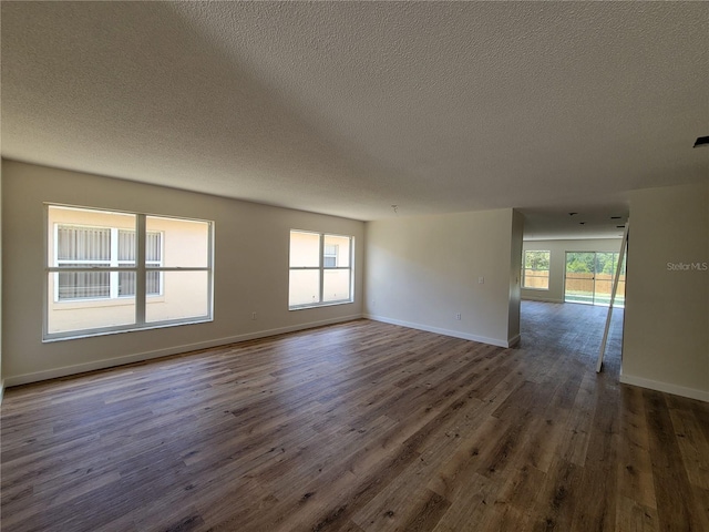 empty room featuring a textured ceiling, dark wood-style floors, and baseboards
