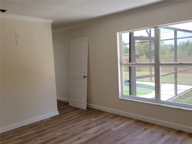empty room with crown molding, wood finished floors, baseboards, and a textured ceiling