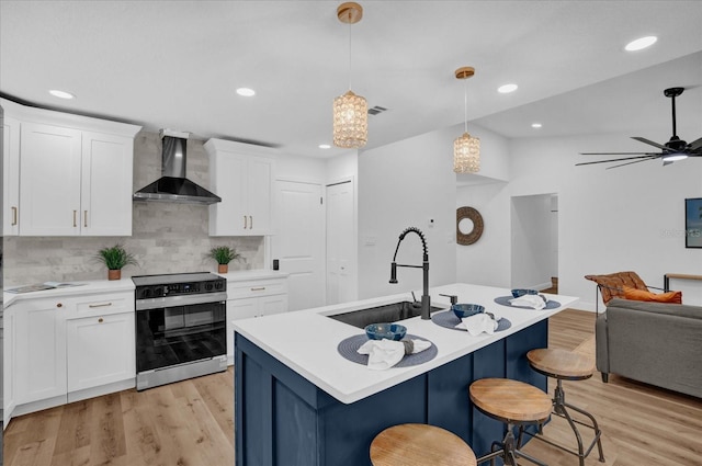 kitchen featuring wall chimney range hood, a sink, electric range, open floor plan, and light countertops