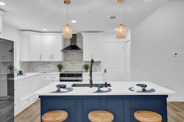 kitchen featuring wall chimney exhaust hood, range with electric cooktop, a sink, a kitchen bar, and recessed lighting