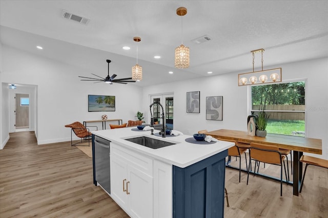 kitchen with a sink, stainless steel dishwasher, light wood-type flooring, white cabinetry, and hanging light fixtures