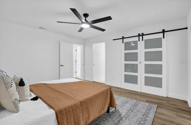 bedroom with a barn door, wood finished floors, baseboards, and ceiling fan