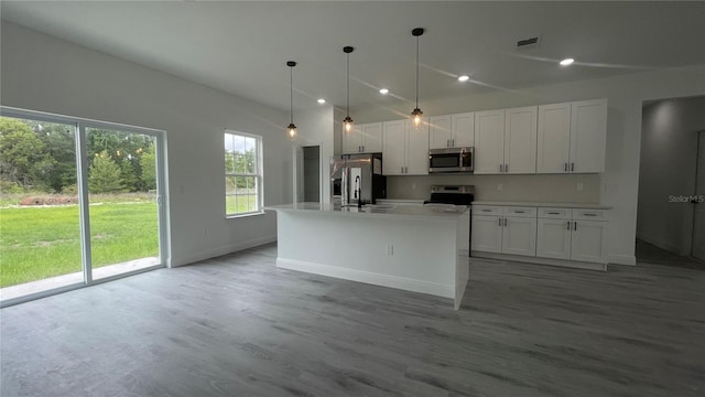 kitchen with appliances with stainless steel finishes, white cabinetry, light countertops, a kitchen island with sink, and light wood-style flooring