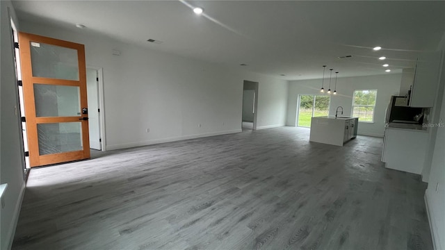 unfurnished living room featuring wood finished floors, baseboards, recessed lighting, and a sink