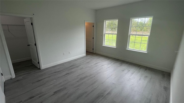 unfurnished bedroom with wood finished floors, baseboards, a spacious closet, and a closet
