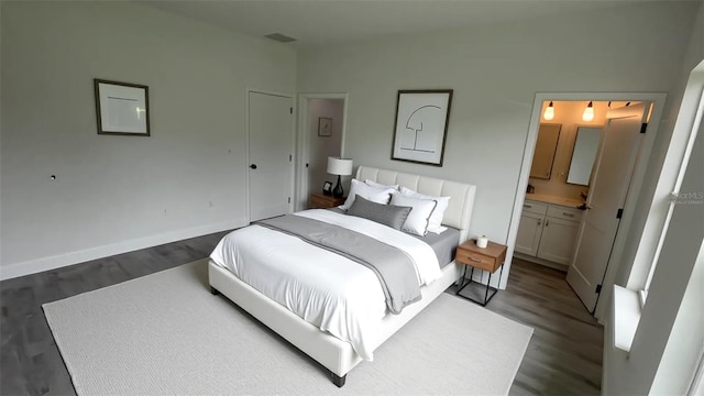 bedroom with dark wood-type flooring, baseboards, and connected bathroom