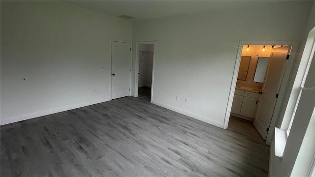 unfurnished bedroom with dark wood finished floors, baseboards, a spacious closet, and ensuite bathroom