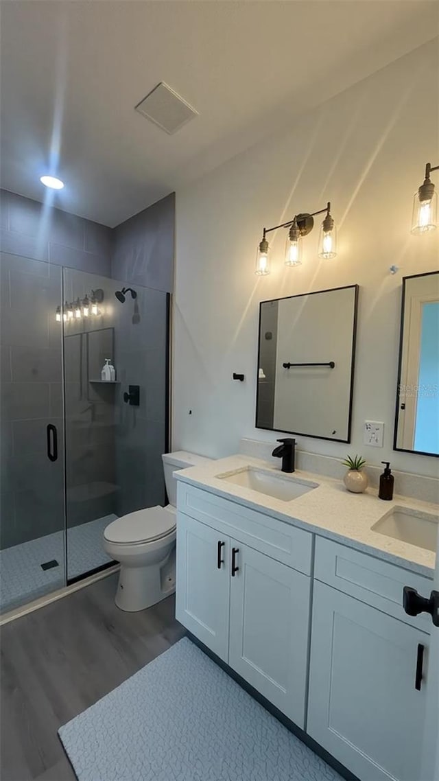 bathroom with a stall shower, wood finished floors, double vanity, and toilet
