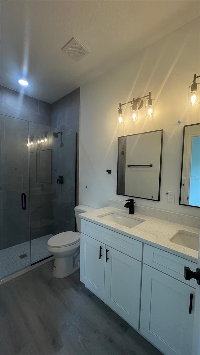 full bathroom with wood finished floors, a shower stall, double vanity, and toilet