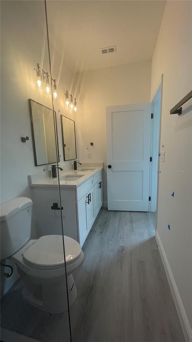 bathroom featuring wood finished floors, toilet, double vanity, and baseboards