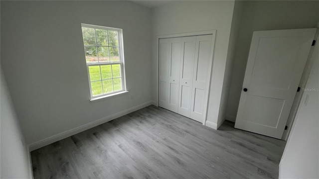 unfurnished bedroom with multiple windows, baseboards, wood finished floors, and a closet