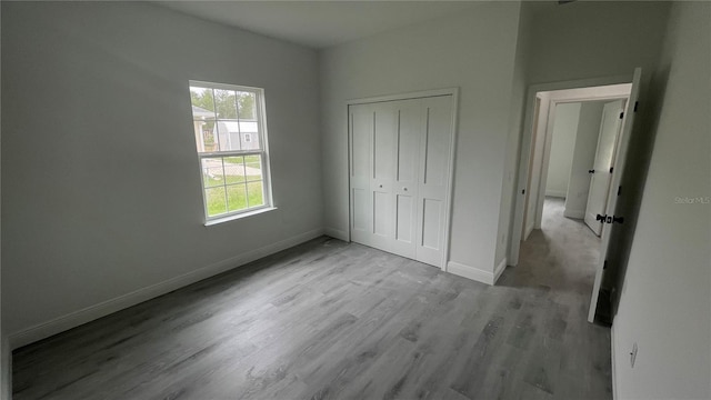 unfurnished bedroom featuring baseboards, wood finished floors, and a closet