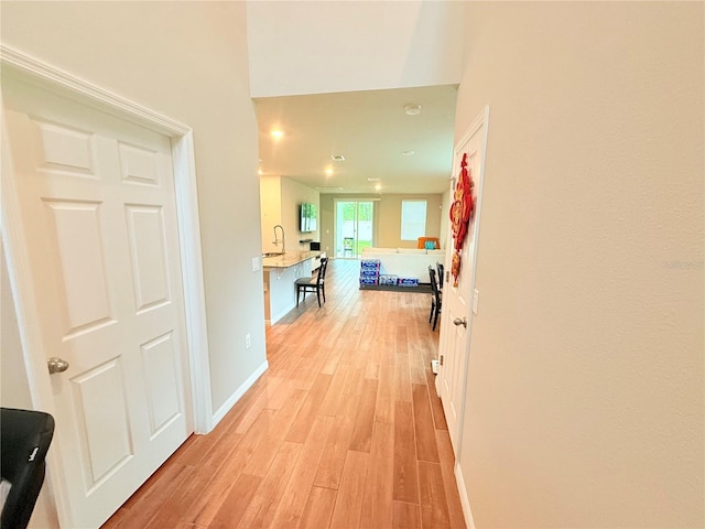 hallway featuring light wood-type flooring, baseboards, and a high ceiling