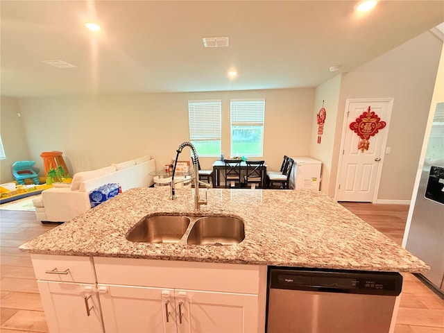 kitchen with stainless steel dishwasher, a sink, open floor plan, light wood-type flooring, and light stone countertops