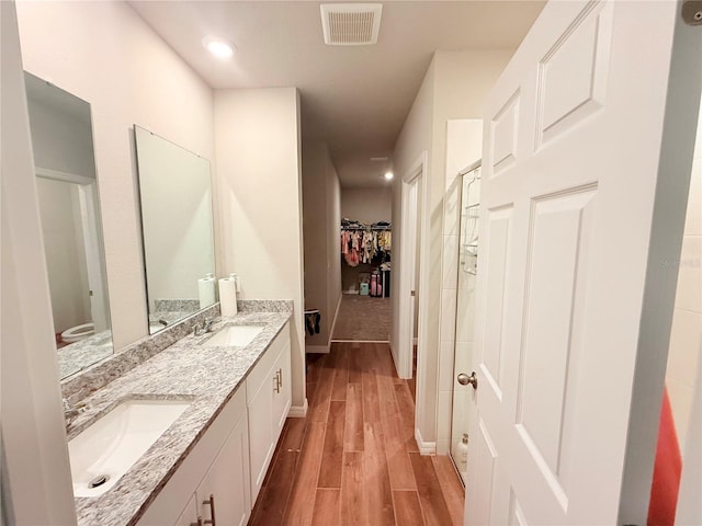bathroom featuring wood finished floors, a walk in closet, double vanity, baseboards, and toilet