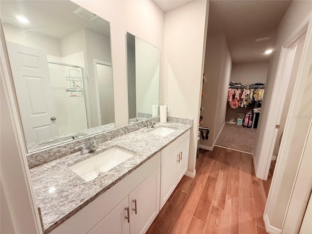 bathroom with wood finished floors, a walk in closet, a stall shower, double vanity, and baseboards
