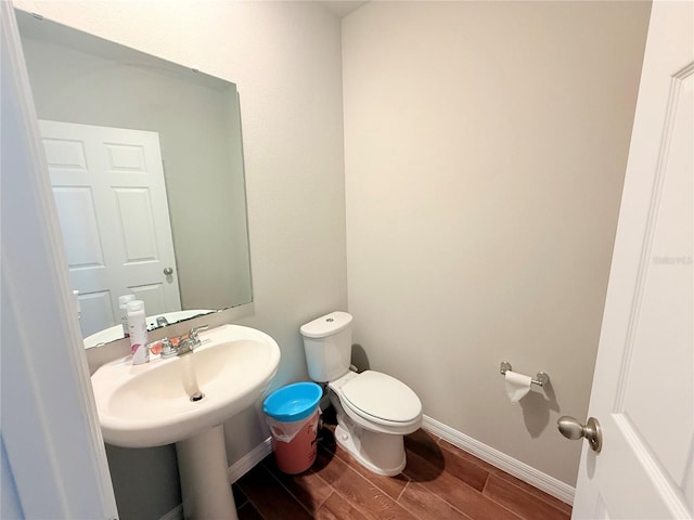 half bathroom featuring wood finished floors, toilet, and baseboards