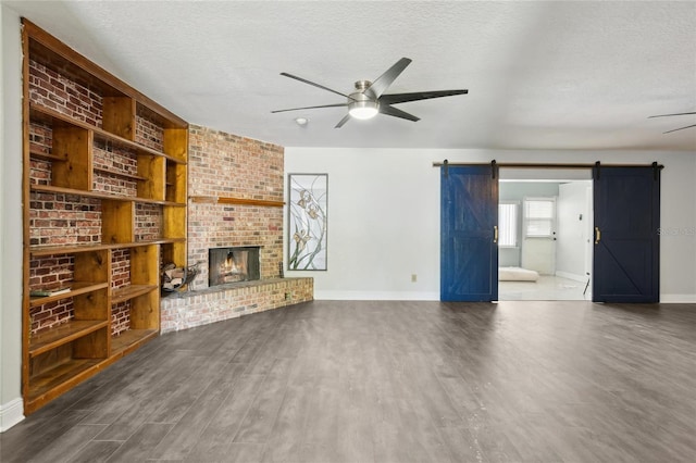unfurnished living room featuring a ceiling fan, a barn door, dark wood finished floors, a textured ceiling, and baseboards