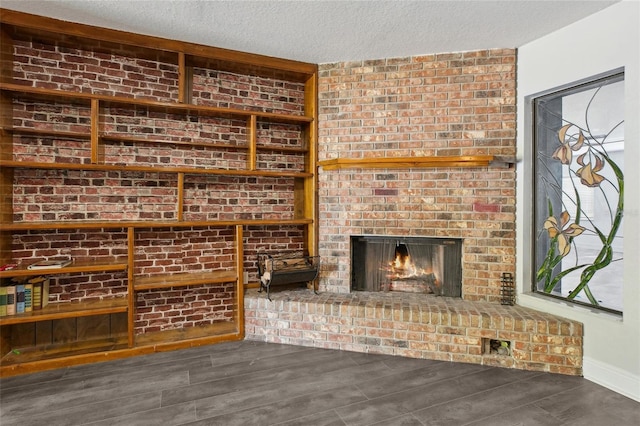 unfurnished living room featuring a fireplace, a textured ceiling, wood finished floors, and baseboards