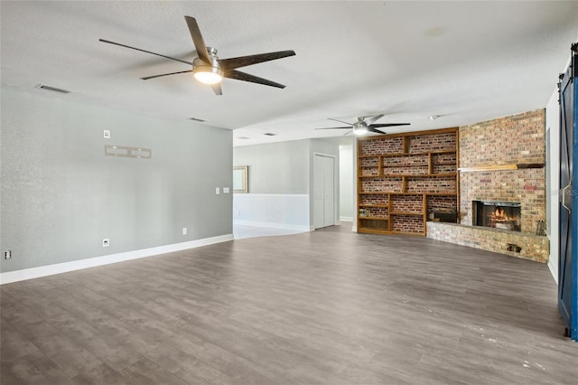 unfurnished living room with a ceiling fan, brick wall, wood finished floors, baseboards, and a textured ceiling