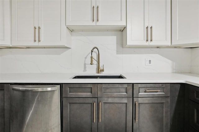 kitchen with stainless steel dishwasher, a sink, light countertops, and white cabinets