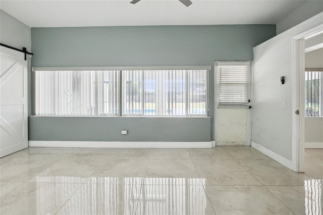 spare room featuring a barn door, baseboards, and a ceiling fan