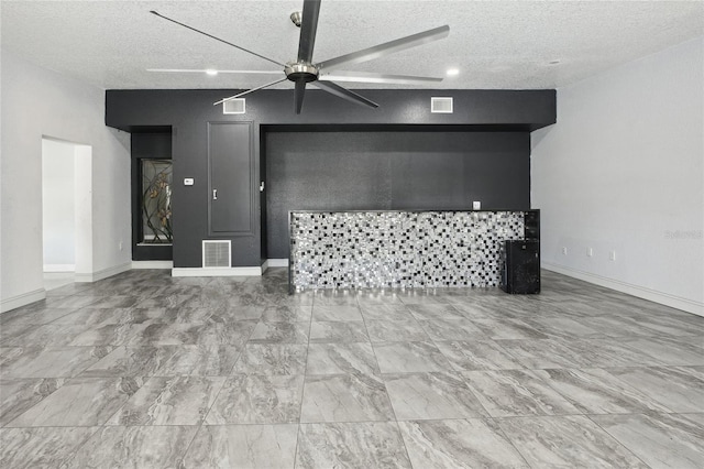 unfurnished living room featuring ceiling fan, a textured ceiling, marble look tile flooring, and baseboards