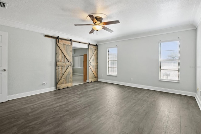 empty room with ceiling fan, a barn door, ornamental molding, a textured ceiling, and dark wood-style flooring