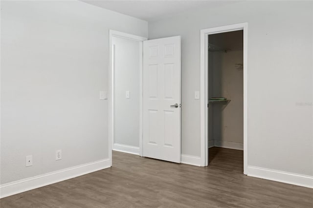 unfurnished bedroom featuring a walk in closet, wood finished floors, baseboards, and a closet