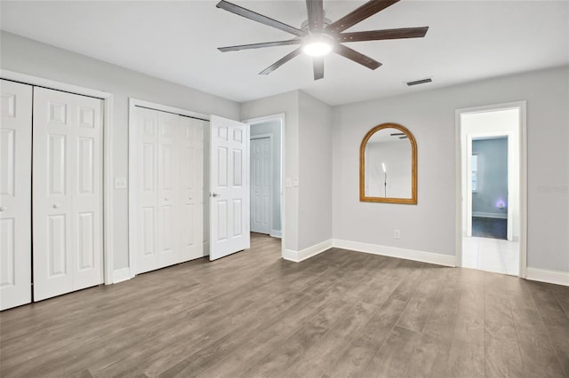 unfurnished bedroom with two closets, wood finished floors, baseboards, and ceiling fan