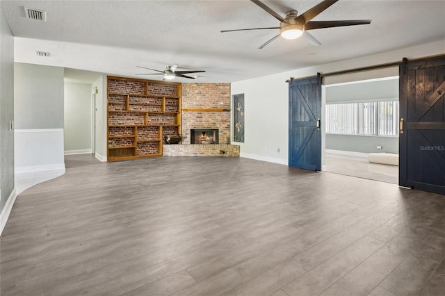 949 Shadow Oaks Rd, Kissimmee, FL 34744 - unfurnished living room featuring a ceiling fan, a barn door, a textured ceiling, wood finished floors, and a fireplace