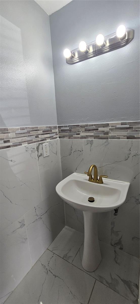 8612 Valley Ridge Ct, Orlando, FL 32818 - bathroom featuring tile walls, marble look tiles, and a wainscoted wall