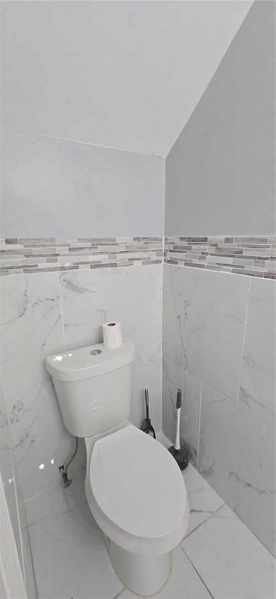 8612 Valley Ridge Ct, Orlando, FL 32818 - bathroom featuring marble finish flooring, tile walls, toilet, and wainscoting