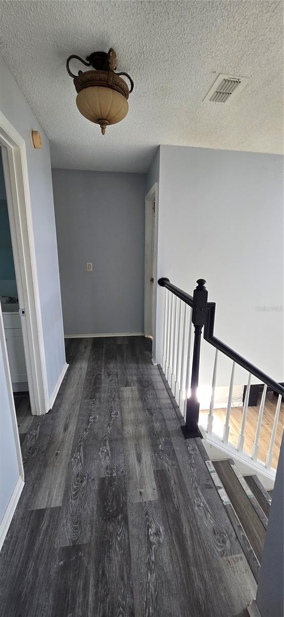 8612 Valley Ridge Ct, Orlando, FL 32818 - hallway featuring wood finished floors, a textured ceiling, an upstairs landing, and baseboards