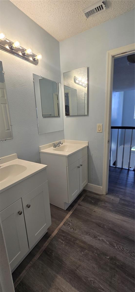 8612 Valley Ridge Ct, Orlando, FL 32818 - bathroom with wood finished floors, a textured ceiling, two vanities, and baseboards