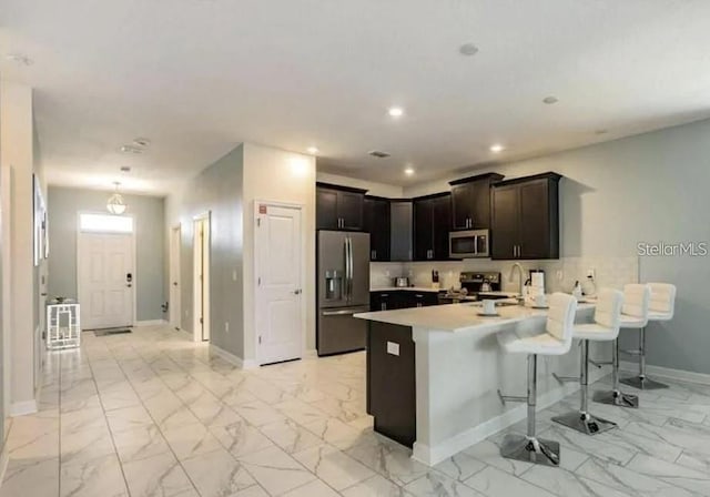 1575 Plunker Dr, Davenport, FL 33896 - kitchen featuring stainless steel appliances, a peninsula, a breakfast bar, light marble finish flooring, and light countertops