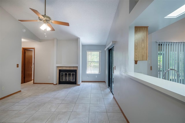 unfurnished living room featuring lofted ceiling, a fireplace, ceiling fan, baseboards, and light tile patterned floors