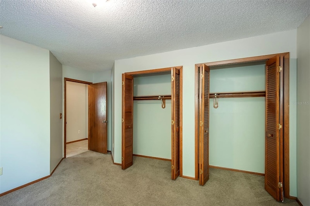 unfurnished bedroom featuring multiple closets, carpet flooring, a textured ceiling, and baseboards
