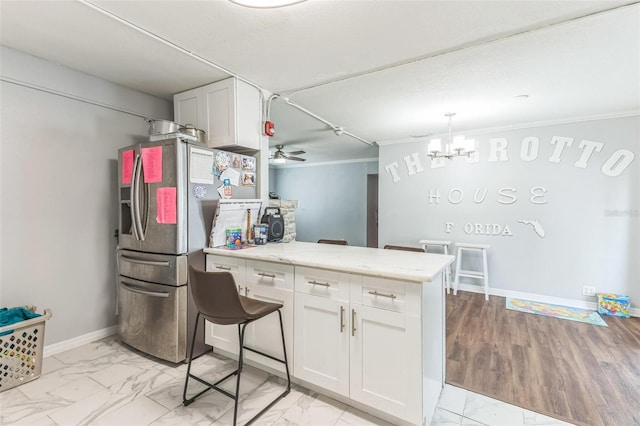 kitchen featuring a peninsula, light marble finish floors, ornamental molding, white cabinets, and a chandelier