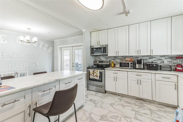 kitchen featuring appliances with stainless steel finishes, light countertops, a chandelier, ornamental molding, and backsplash