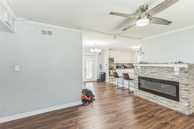 living room featuring ornamental molding, dark wood-type flooring, ceiling fan, baseboards, and a stone fireplace