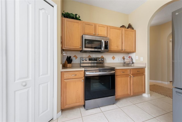 5007 Bellthorn Dr, Orlando, FL 32837 - kitchen featuring stainless steel appliances, arched walkways, light countertops, decorative backsplash, and light tile patterned flooring