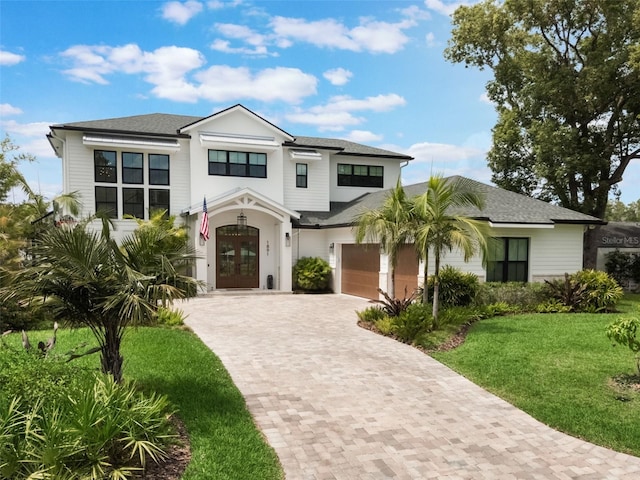 view of front of property with decorative driveway, french doors, a front lawn, a garage, and a shingled roof