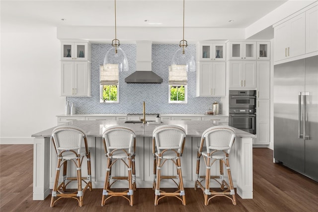 kitchen with appliances with stainless steel finishes, wall chimney exhaust hood, a center island with sink, and backsplash