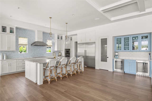 kitchen with wine cooler, appliances with stainless steel finishes, wall chimney exhaust hood, backsplash, and recessed lighting