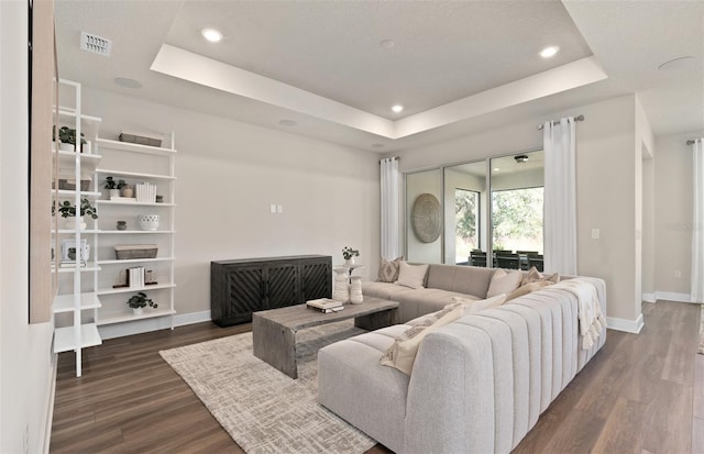living room featuring a tray ceiling, baseboards, dark wood-type flooring, and recessed lighting