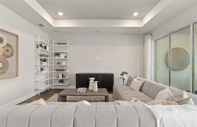 living room featuring dark wood-style flooring, baseboards, a raised ceiling, and recessed lighting