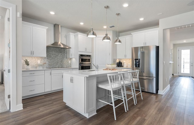 kitchen featuring appliances with stainless steel finishes, wall chimney exhaust hood, an island with sink, white cabinetry, and recessed lighting